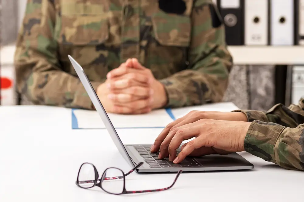 Officier militaire en entretien de recrutement face à un candidat utilisant un ordinateur portable dans un bureau.