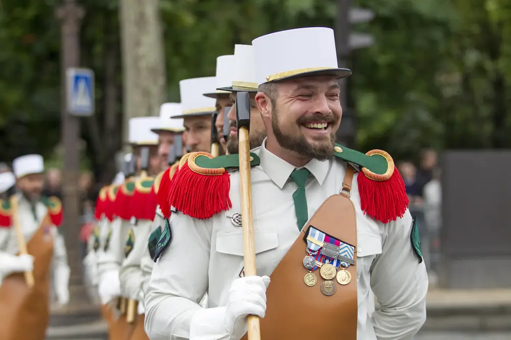 Pionniers de la Légion étrangère barbus en tenue de parade avec képi blanc, tablier de cuir et hache sur l'épaule.