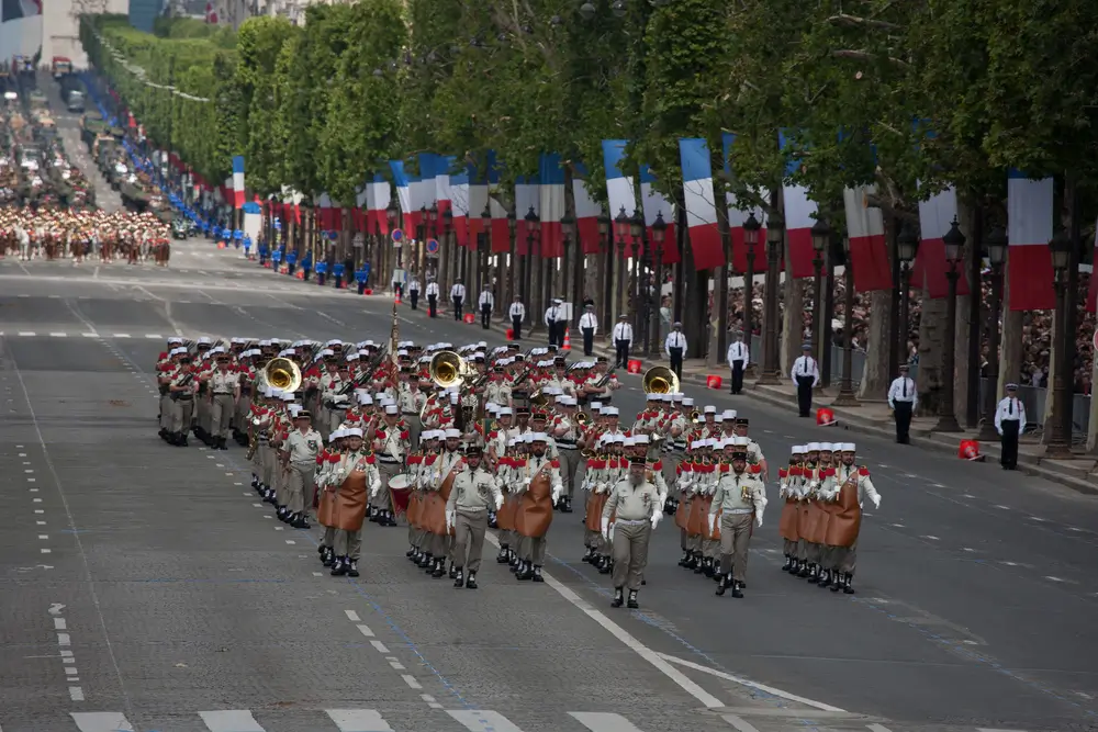 Défilé des soldats de la Légion étrangère en uniforme traditionnel avec képis blancs et tabliers de cuir des pionniers.