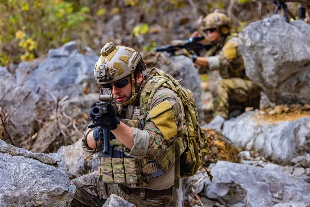 Soldats en plein entraînement militaire sur un terrain rocheux, équipés de casques et de fusils d'assaut.