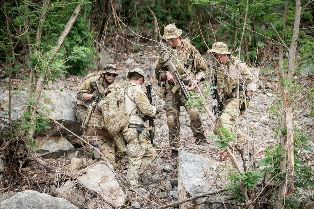 Légionnaires en tenue de combat effectuant une patrouille en forêt avec leurs fusils et équipements militaires.