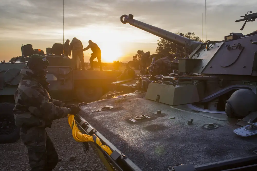Pionnier militaire de la Légion étrangère en uniforme de combat préparant un véhicule blindé au lever du soleil.