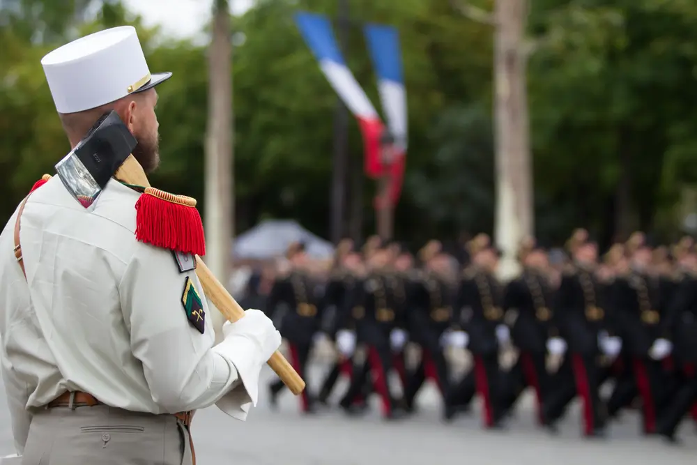 Légionnaire pionnier en képi blanc avec une hache à l'épaule lors d'un défilé militaire en formation.