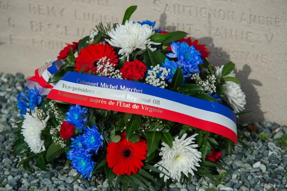 Gerbe de fleurs tricolores déposée devant un monument aux morts gravé lors d'une cérémonie de commémoration militaire.
