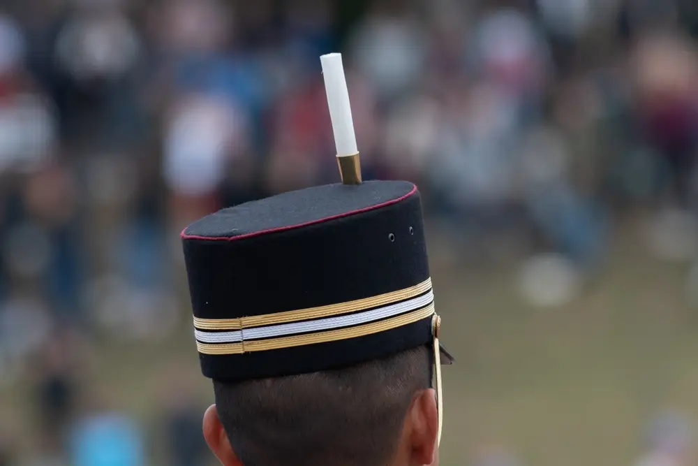 Képi de la Légion étrangère avec galons et plumet blanc, coiffe militaire française portée par un soldat de dos.