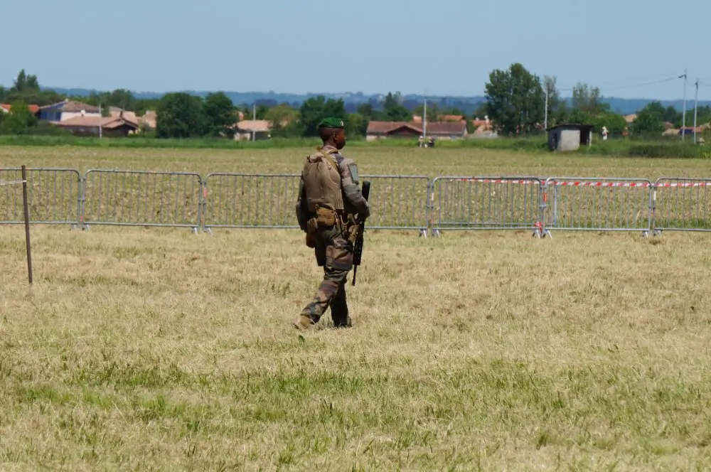 Légionnaire en tenue de combat et béret vert patrouillant dans un champ lors d'une mission opérationnelle.