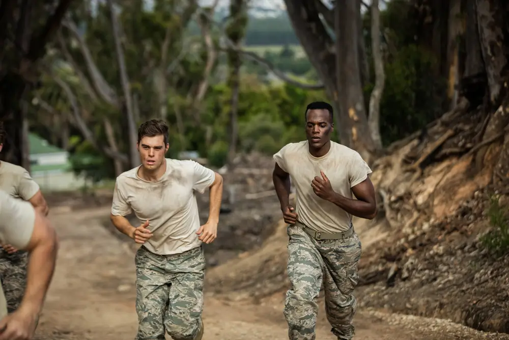 Deux soldats en treillis et t-shirt beige courent sur un chemin terreux lors d'un entraînement militaire sportif.