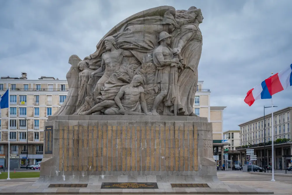 Monument aux morts militaire avec sculptures allégoriques et listes de noms gravées en or, encadré par des drapeaux.