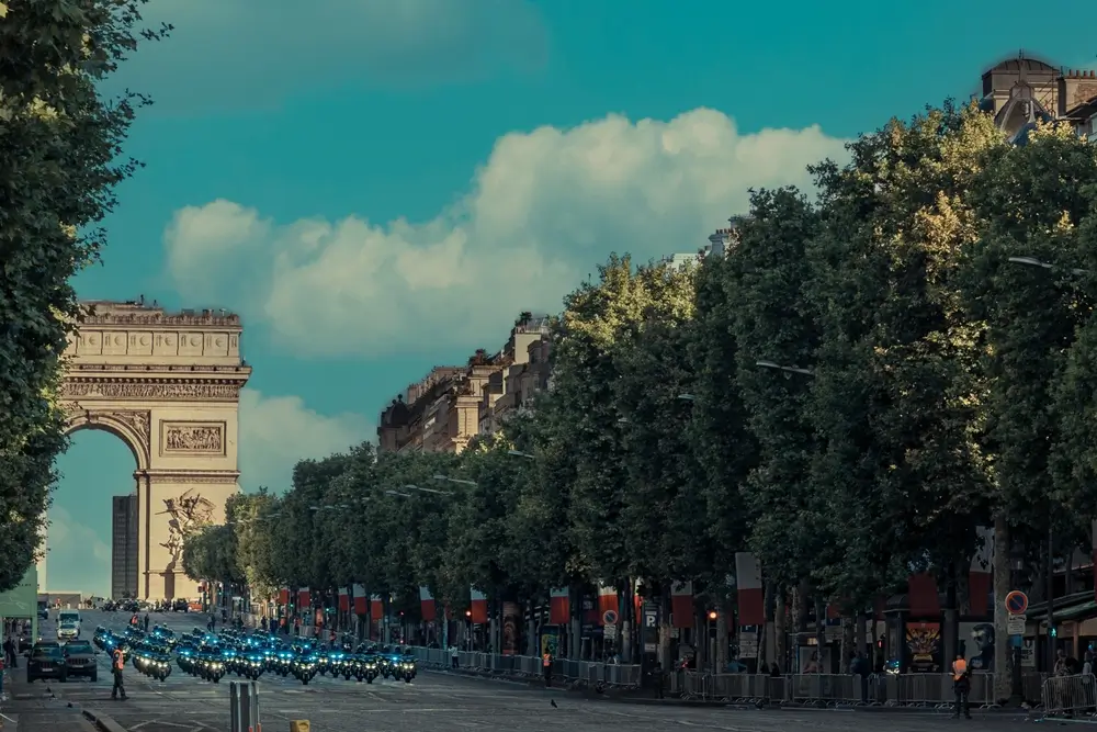 Défilé militaire de soldats à moto sur les Champs-Élysées avec l'Arc de Triomphe en arrière-plan.