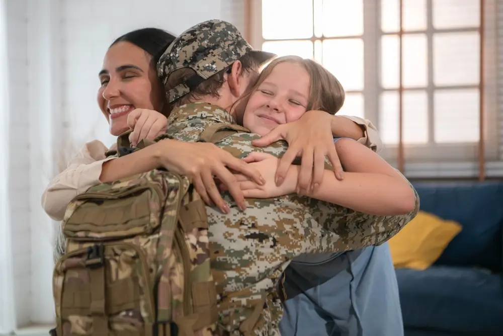 Un militaire en uniforme enlace chaleureusement sa femme et sa fille lors de retrouvailles après une mission.